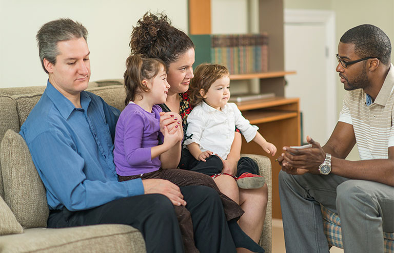 Photo of a family of four sitting on couch speaking to a childcare specialist