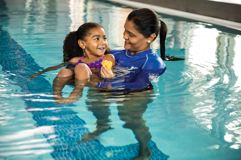 Photo of a YMCA swimming instructor teaching a YMCA youth member how to swim in a swimming pool