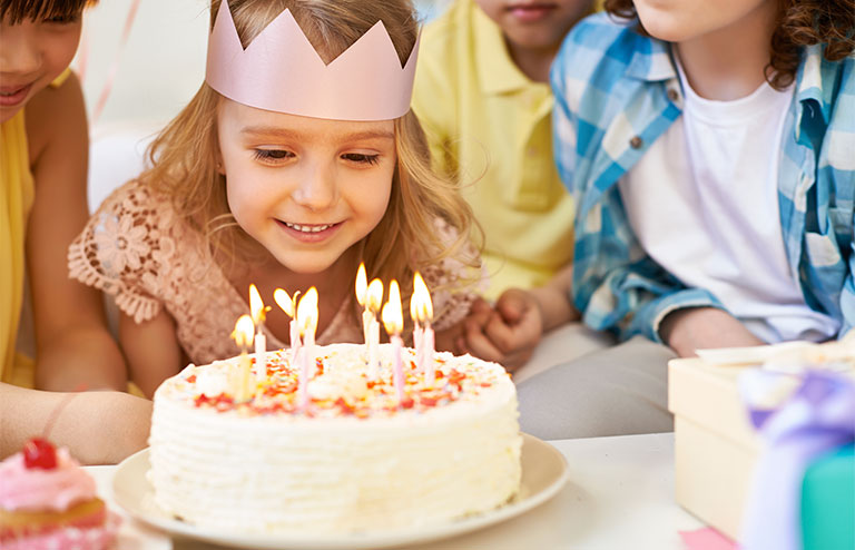 Photo of a girl wearing a crown preparing to blow candles on her birthday cake