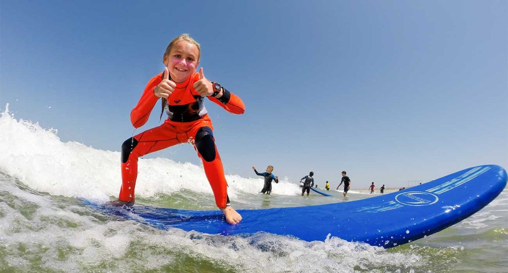 Photo of a camp surfer riding a surfboard giving a thumbs-up