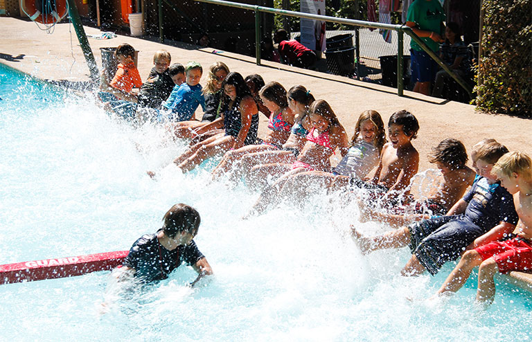 Photo of kids sitting on the side of the pool creating waves