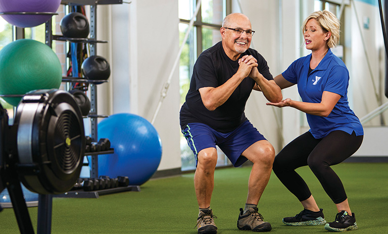 Photo of an exercise instructor helping a YMCA member do a squat