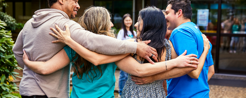 Photo of four adults with their arms around each others' shoulders