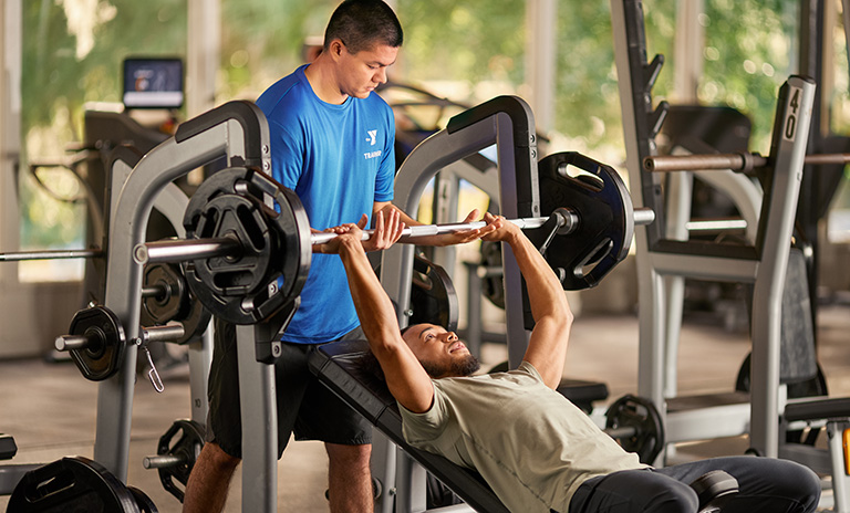 Photo of a YMCA trainer helping a YMCA member with the incline bench press exercise machine