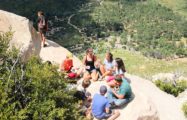 Photo of a gathering of YMCA members sitting in a circle on a cliffside of a mountain