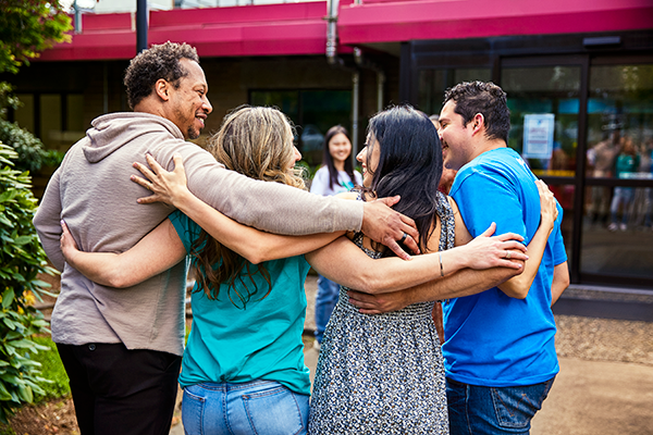 Photo of four adults with their arms around each others' shoulders