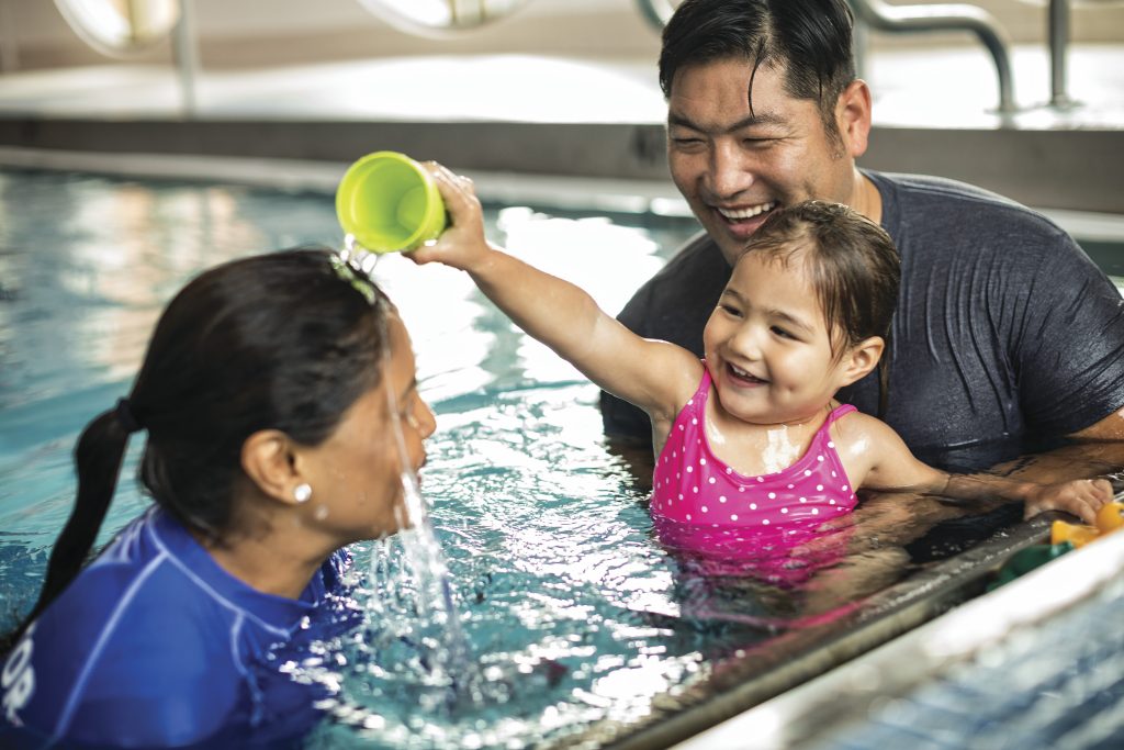 Father and daughter taking swimming lessons, dumping water on the instructor's head.