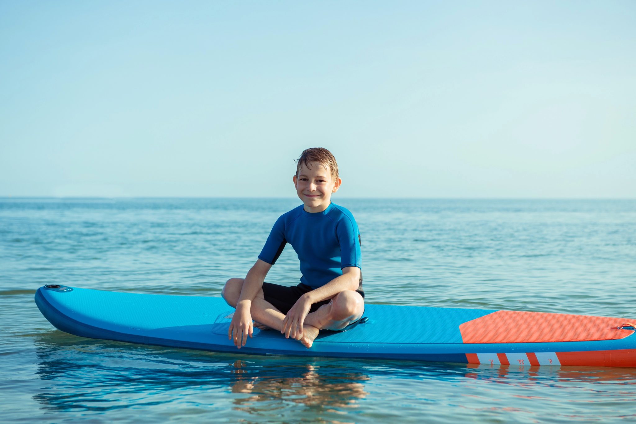 Boy smiling and sitting on a blue paddleboard on the water