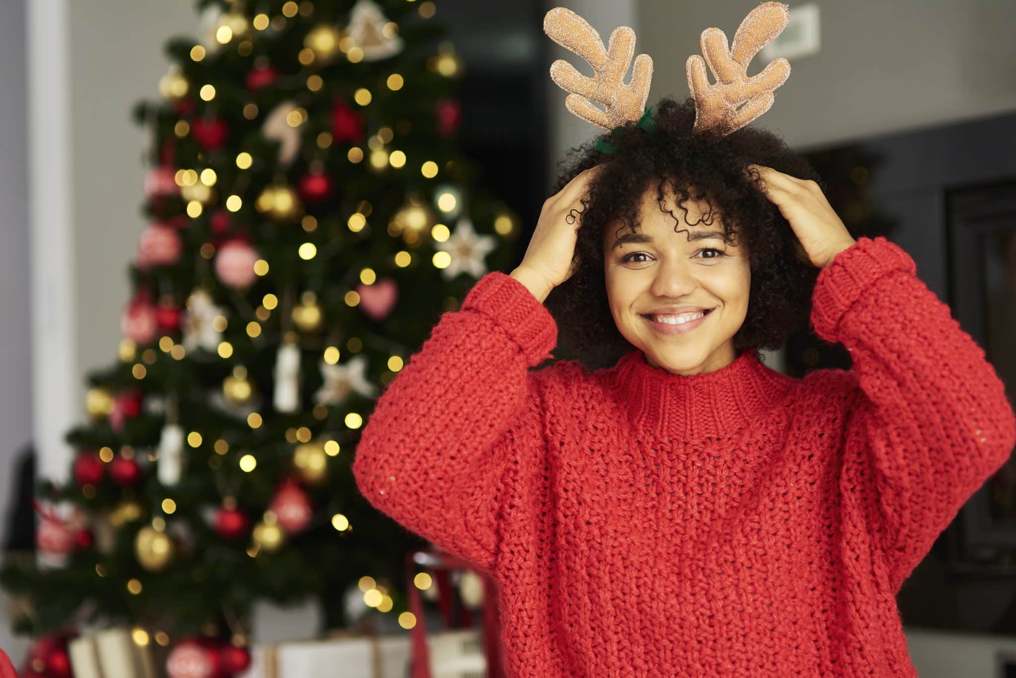 Woman with reindeer antlers by a decorated tree.